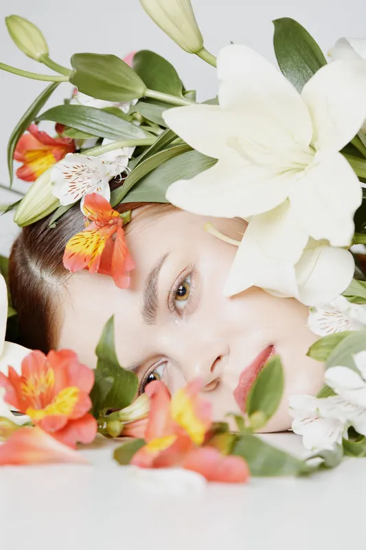 Fresh and vibrant portrait of a young woman surrounded by colorful flowers, reflecting beauty, serenity, and nature, ideal for promoting natural skincare or wellness concepts
