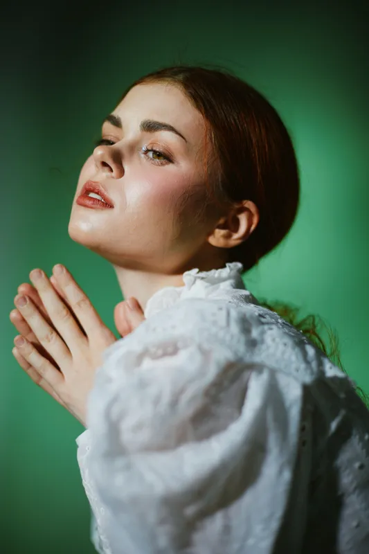 Female model in vintage white dress against a green background, expressing serenity and grace, showcasing natural beauty and soft emotions