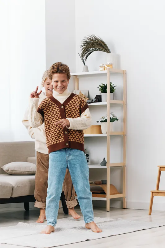 Authenticity shines in a playful home scene with a smiling child and caregiver, school themed knitwear, cozy setting, and a warm lifestyle moment.