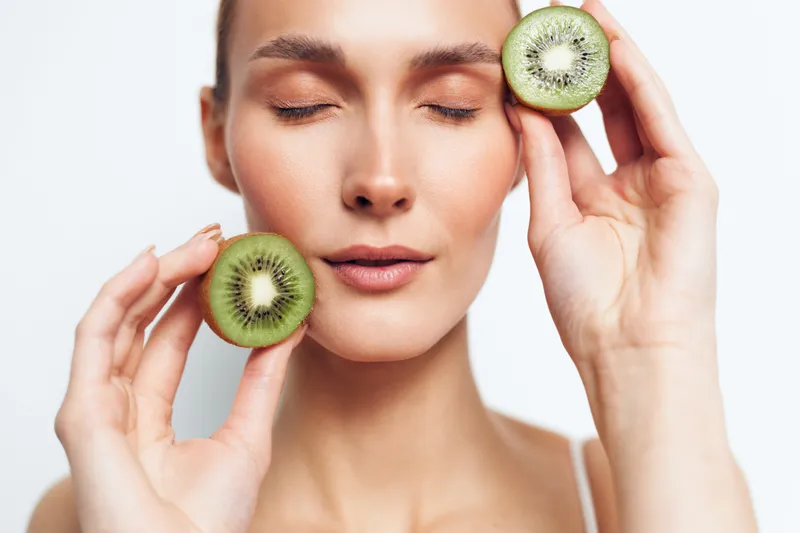 Woman kiwi skincare fruit spa studio freshness wellness beauty closeup, holding kiwi slices for facial care, eyesclosed serene relaxation, soft natural light, white background