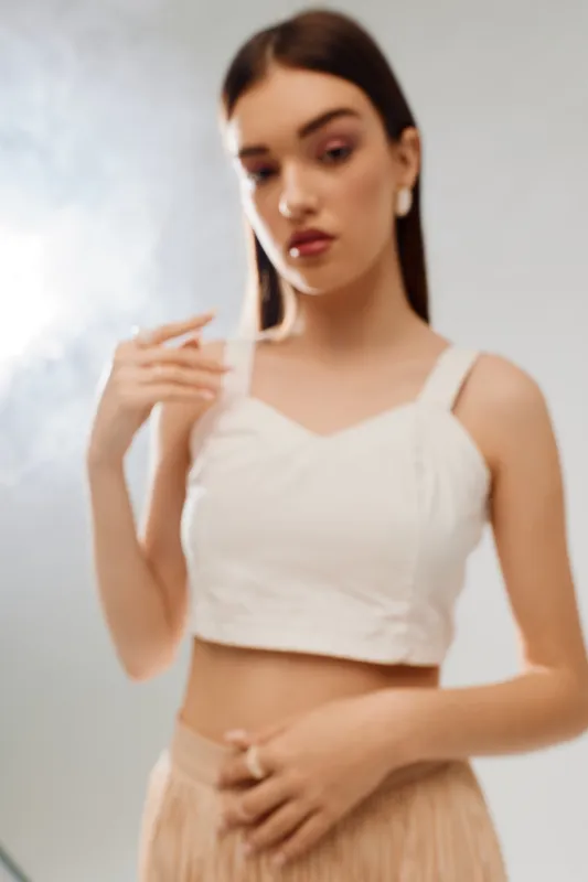 Young woman in white top and beige skirt poses with soft expression in studio. Blurred background creates gentle mood. Concept for woman beauty fashion and elegance.