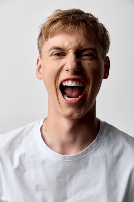 Yelling man in a white tee, open mouth and intense expression conveying sudden excitement, energy and raw emotion for bold marketing, social media, or ad campaigns