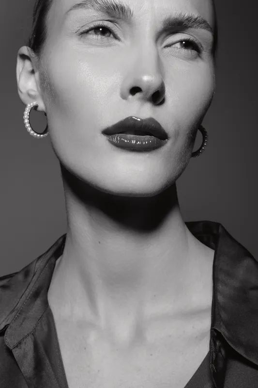 Close-up of white woman with light skin and dark lipstick posing with serious expression in black and white studio portrait.