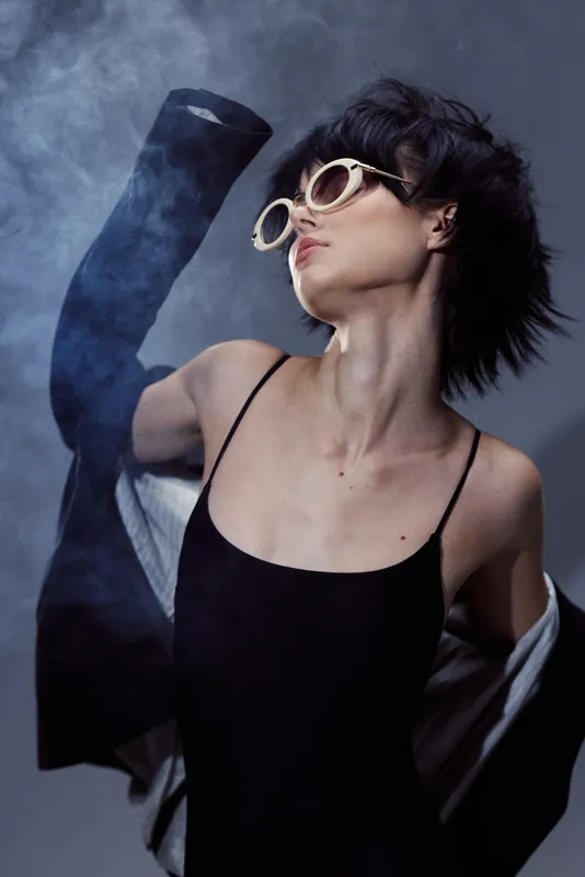 Stylish woman wearing black dress and sunglasses posing confidently with smoky background and dynamic movement
