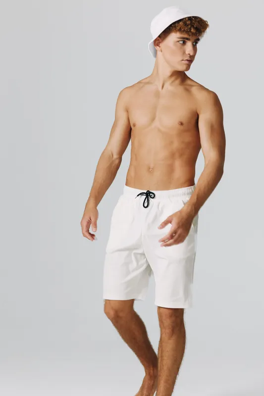 Young shirtless man wearing white shorts and white cap looking to side isolated on gray studio background with barefoot standing relaxed with athletic body.