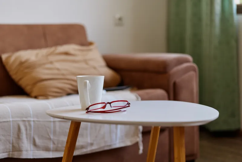 Cozy living room scene with a round coffee table, a cup and reading glasses, soft natural light, relaxed mood, plush sofa, warm neutrals, candid home lifestyle moment in a calm interior