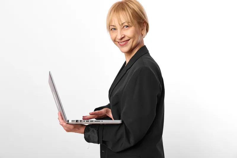 Smiling older woman holding laptop in office setting, confident business and technology concept, portrait on white background, ready for remote work, with computer skills today