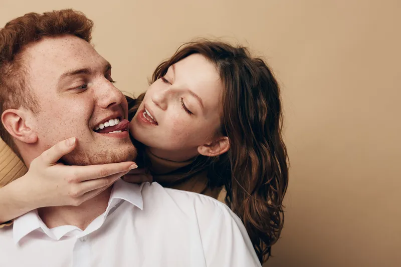 Happy young couple embraces and smiles in close-up on beige background. Intimate moment of love, affection, and connection between man and woman in casual clothing.