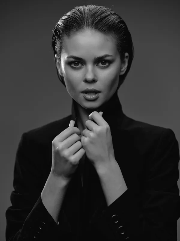 Black and white portrait of a serious woman in a blazer with slicked back hair expressing intensity and confidence.