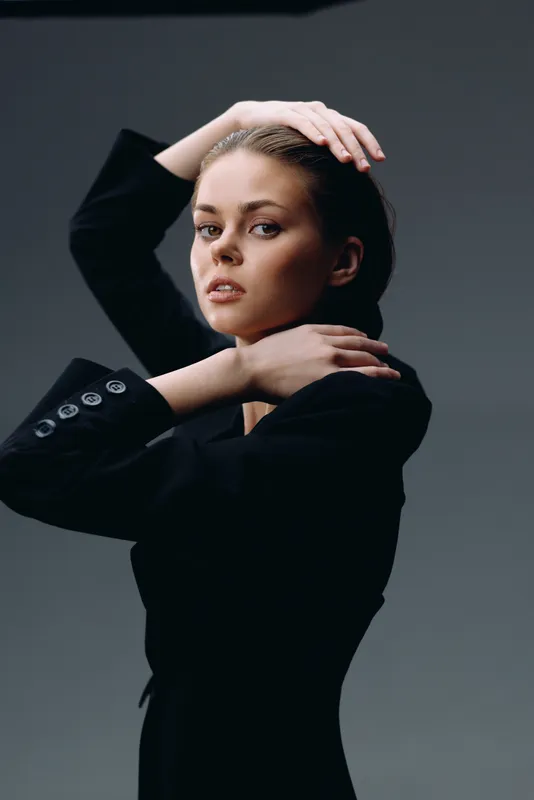 Young woman posing in black outfit with confident expression on gray background