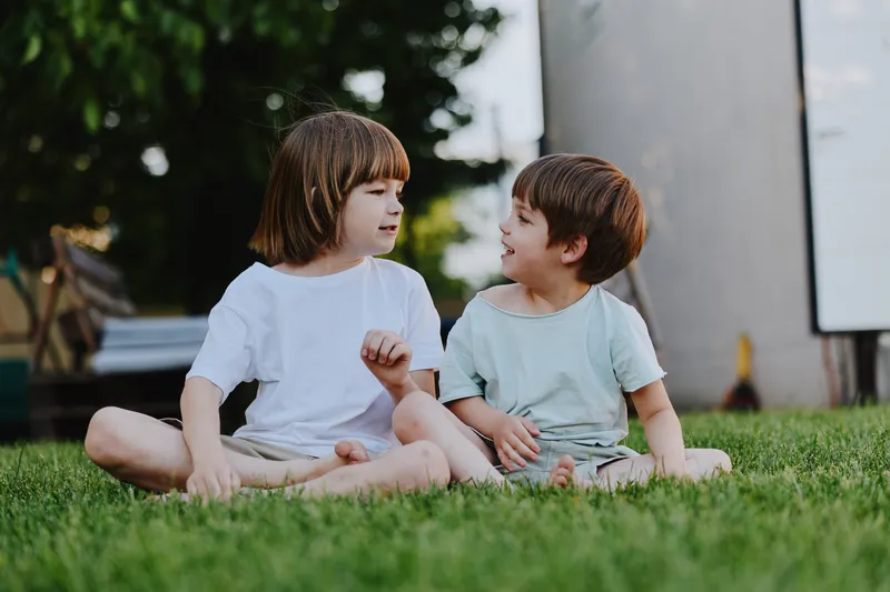 Two children enjoying a sunny day outdoors, playing and laughing on green grass, embodying youthful joy and friendship.