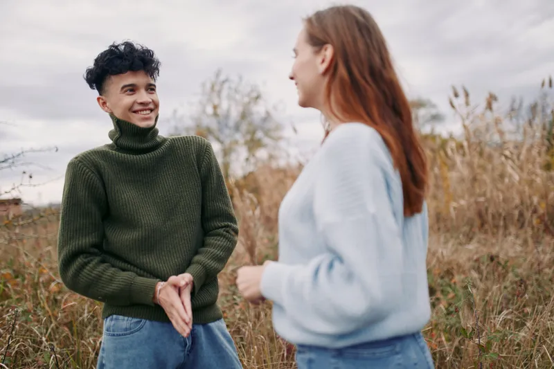 A candid outdoor portrait of two friends sharing a warm moment in a grassy field, natural smiles and relaxed body language convey authenticity and subtle credibility in everyday connection.