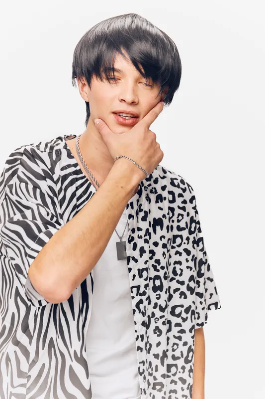 Young man with stylish black hair wearing mixed animal print shirt, posing thoughtfully against a white background with casual and modern fashion vibe.