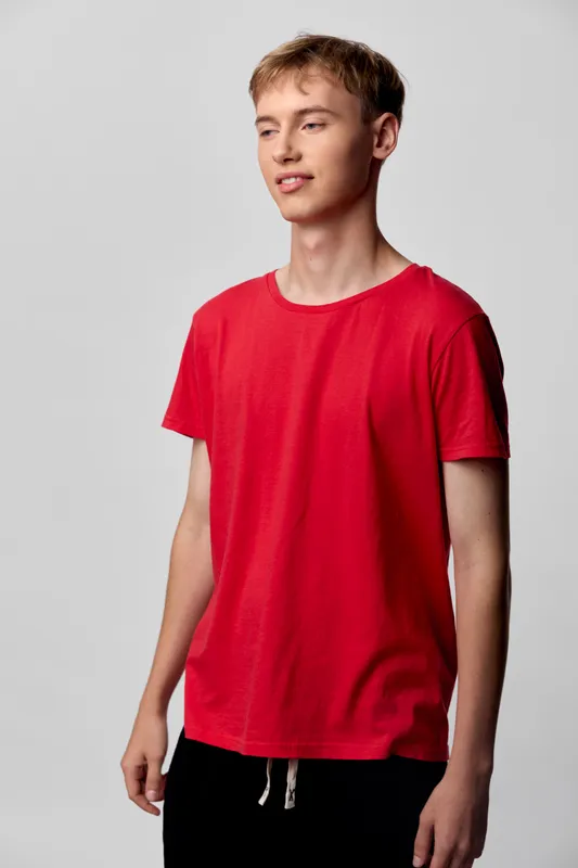 Teen boy in a red t shirt stands in a neutral studio, showcasing casual fashion and relaxed pose perfect for youth apparel, lifestyle visuals, and everyday wear concepts