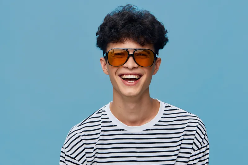 smiling man with sunglasses wearing striped shirt against blue background, happy expression, casual style, youthful look, bright lighting