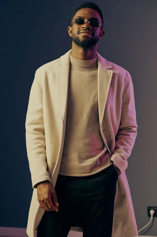 Stylish man in a modern coat and sunglasses, exuding confidence against a colorful backdrop Fashion and elegance in contemporary clothing