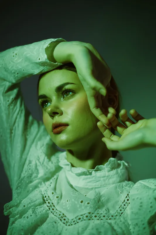 Elegant woman in white vintage dress, expressing contemplation with green lighting, ideal for concepts of fashion, beauty, or emotion