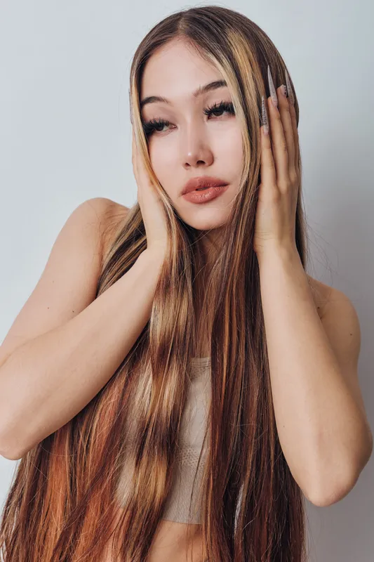 Woman with long straight hair and natural makeup posing with hands near face on light background. Beauty, fashion, hairstyle and portrait with soft lighting and casual style.