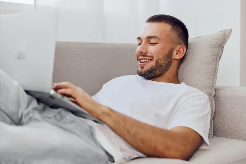 Relaxed man enjoying remote work on a laptop, showcasing emotional well-being and the balance between personal and professional life. Concepts of mental health and technology use.