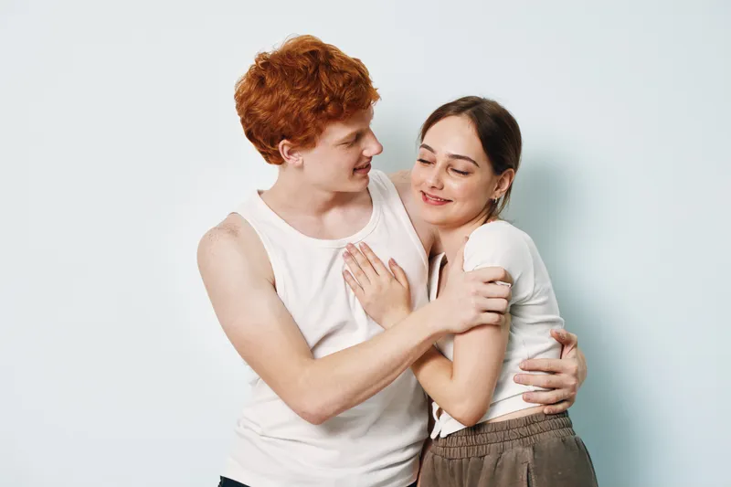 Couple embracing and smiling with affection, young man and woman in casual clothes showing love and connection against plain background in studio.