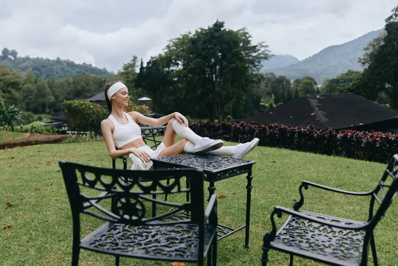 Fit young woman relaxing outdoors in sportswear, enjoying nature on a sunny day, showcasing a healthy lifestyle and wellness concept in a serene garden setting