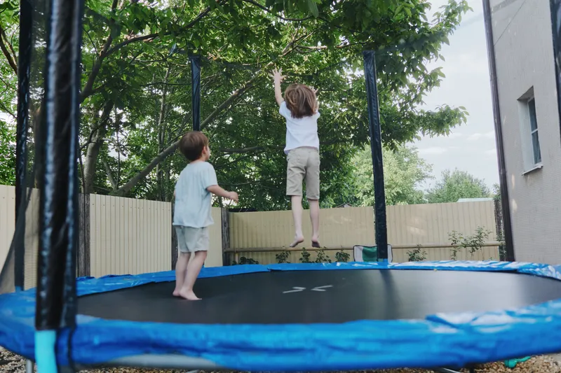 Happy children jumping on a trampoline, enjoying outdoor playtime with green trees in the background, capturing the essence of childhood joy and freedom.