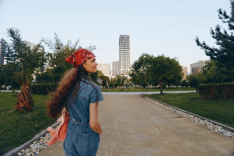lifestyle woman in modern boho-western denim street style stands relaxed outdoors with urban greenery and buildings, captured in warm film color tones for vintage feel