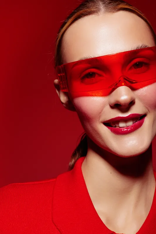 Close-up of smiling woman wearing red sunglasses and red outfit on red background. Fashion portrait with vibrant colors and confident expression. Concept of style and modern look.