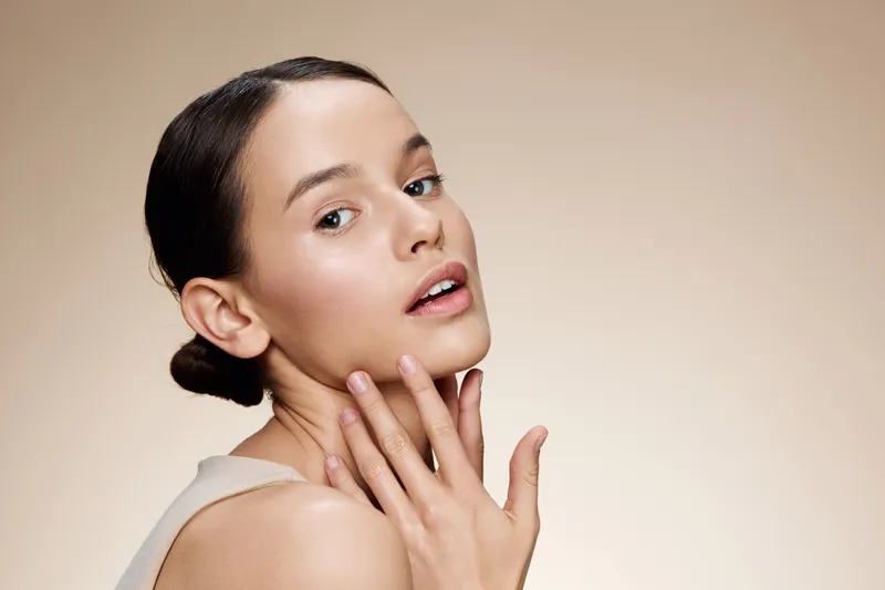 Elegant young woman with clear skin showcasing beauty against a soft neutral background, emphasizing natural beauty and self care