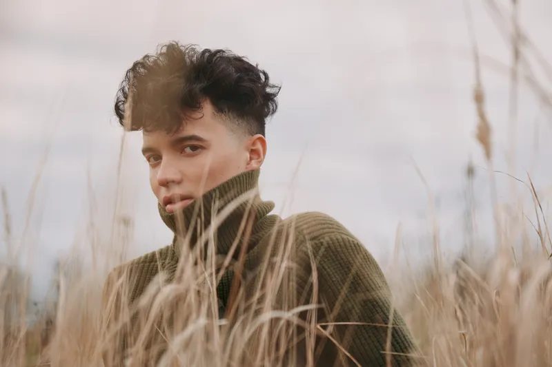 A candid portrait of a young man in tall grass, displaying authentic expression and natural texture under soft outdoor light, capturing a genuine moment.
