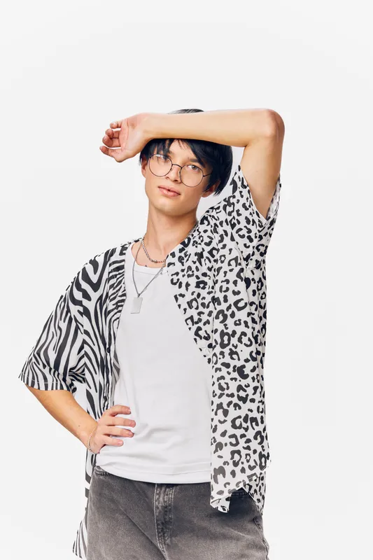 young man wearing animal print shirt and glasses posing confidently against white background with casual style and modern look