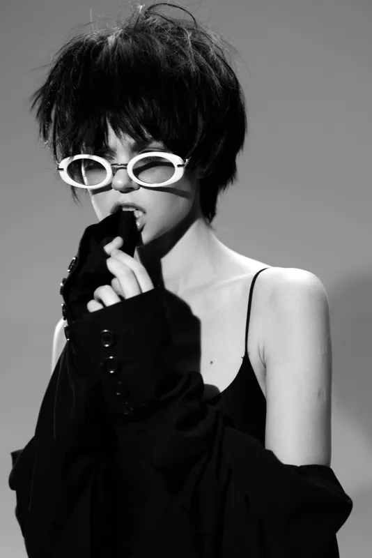 young woman in stylish sunglasses wearing black clothing in black and white artistic portrait