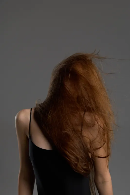 woman with long red hair in black top against gray background, mysterious and dramatic portrait