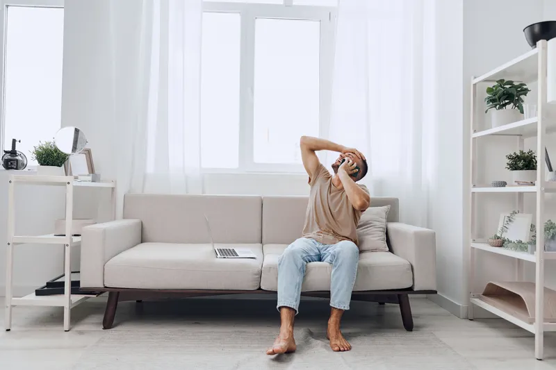 Thoughtful man relaxing at home with a laptop, expressing moments of introspection and creativity in a cozy, minimalistic living space.