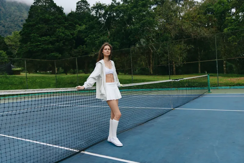 Young athletic woman in stylish sportswear posing on tennis court, showcasing confidence and elegance, surrounded by a natural green backdrop