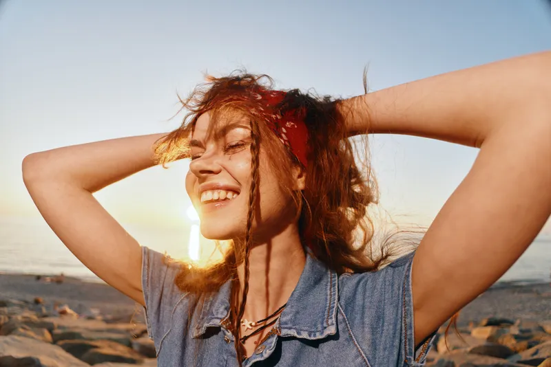 Lifestyle woman enjoying sunny beach sunset in modern boho-western denim street style with film color warmth and carefree happiness outdoors.
