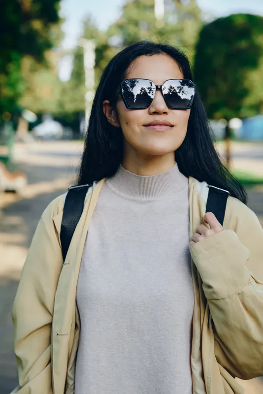 Sunglasses, woman and casual outerwear in sunny park setting, fashion sense shown in light jacket and backpack, outdoor lifestyle and relaxed mood