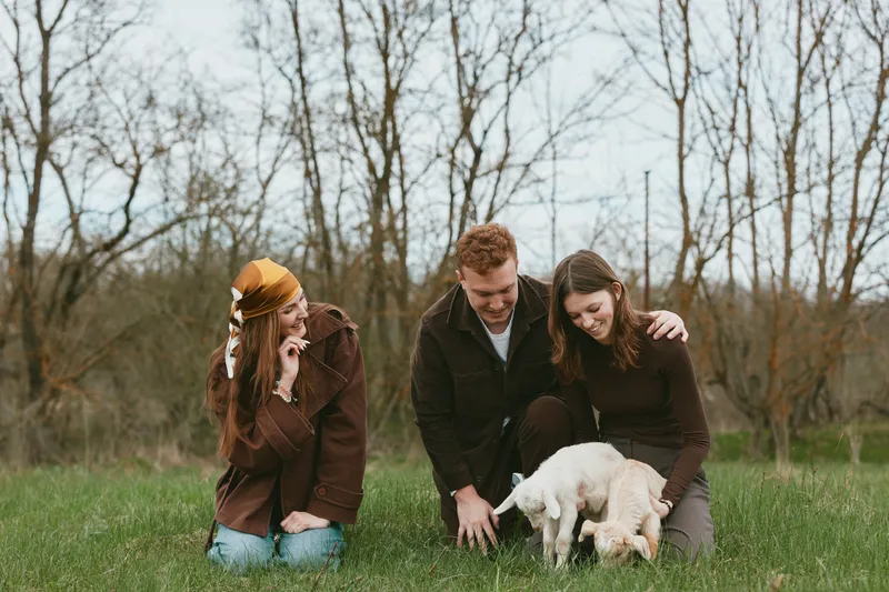 Family goat kid outdoors in a bright meadow, smiles and gentle touch as a small animal explores with a cheerful group. A warm countryside moment highlighting companionship, nature, and everyday farm