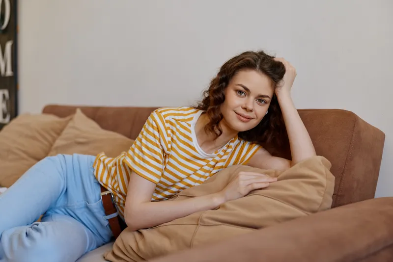 Relaxed woman lounging on a sofa at home, wearing a striped t shirt and jeans. Close up on a cozy living space, showcasing comfort, casual style, and a warm, inviting mood.