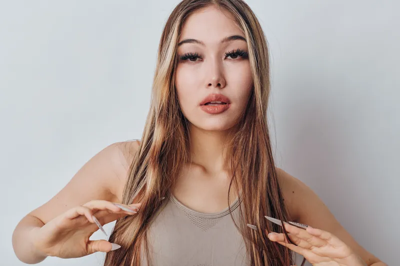 Young woman with long hair and natural makeup in tank top posing against white background for beauty, fashion and lifestyle portrait with casual style and confident expression.