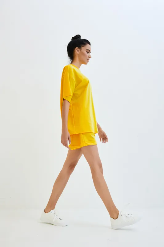 Woman walking confidently in bright yellow casual outfit against white background, showcasing sporty style and relaxed mood in vibrant color palette.