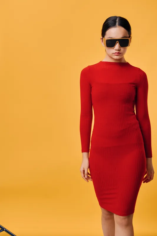 Woman wearing red dress and sunglasses posing on orange background studio. Fashion model with long sleeves and casual style stands confidently with minimal expression and straight hair.