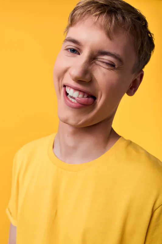 Smiling, winking youth in a vivid yellow shirt against a bright backdrop, conveying cheerful energy, playful mood and upbeat vibe for lifestyle, fashion and positivity campaigns