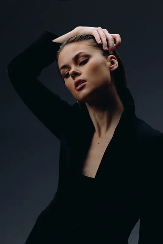 Elegant woman posing in black outfit with dramatic lighting and dark background