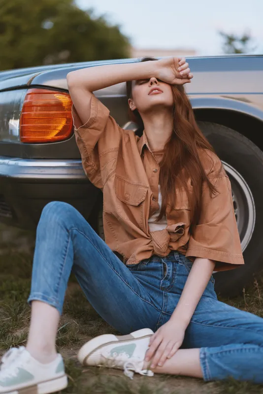 Stylish young woman in casual clothing posing next to a vintage car during a sunny day, showcasing a relaxed vibe and trendy fashion with a focus on outdoor lifestyle.