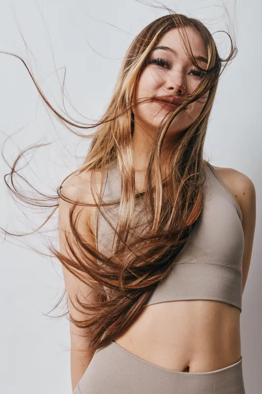 Young woman with long hair wearing sleeveless top and pants posing with hair flowing on white background. Woman, hair, beauty, fashion, model, portrait, smile.