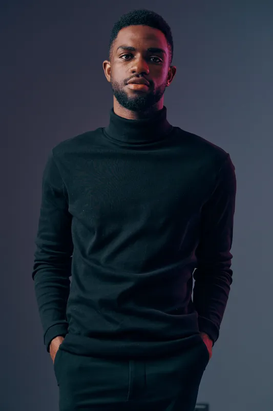 Stylish African man in black turtleneck exuding confidence, with a modern gray background, perfect for fashion or lifestyle concepts