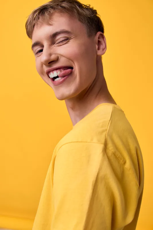 Smiling joy with yellow shirt, playful man in closeup studio shot, cheerful expression captured in bright lighting, a lifestyle fashion vibe perfect for youth and positive branding