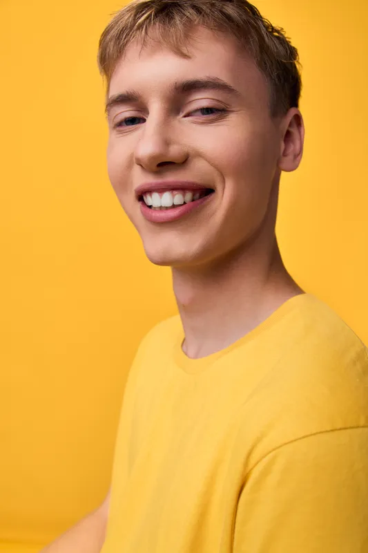 Smiling man in a bright yellow shirt against a yellow studio backdrop, creating a vibrant, cheerful image suitable for lifestyle, fashion, and upbeat branding campaigns