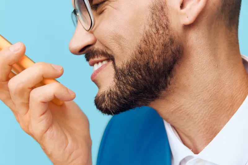 A professional businessman smiles with confidence and emotion against a solid blue background, conveying leadership, communication, and modern work presence.